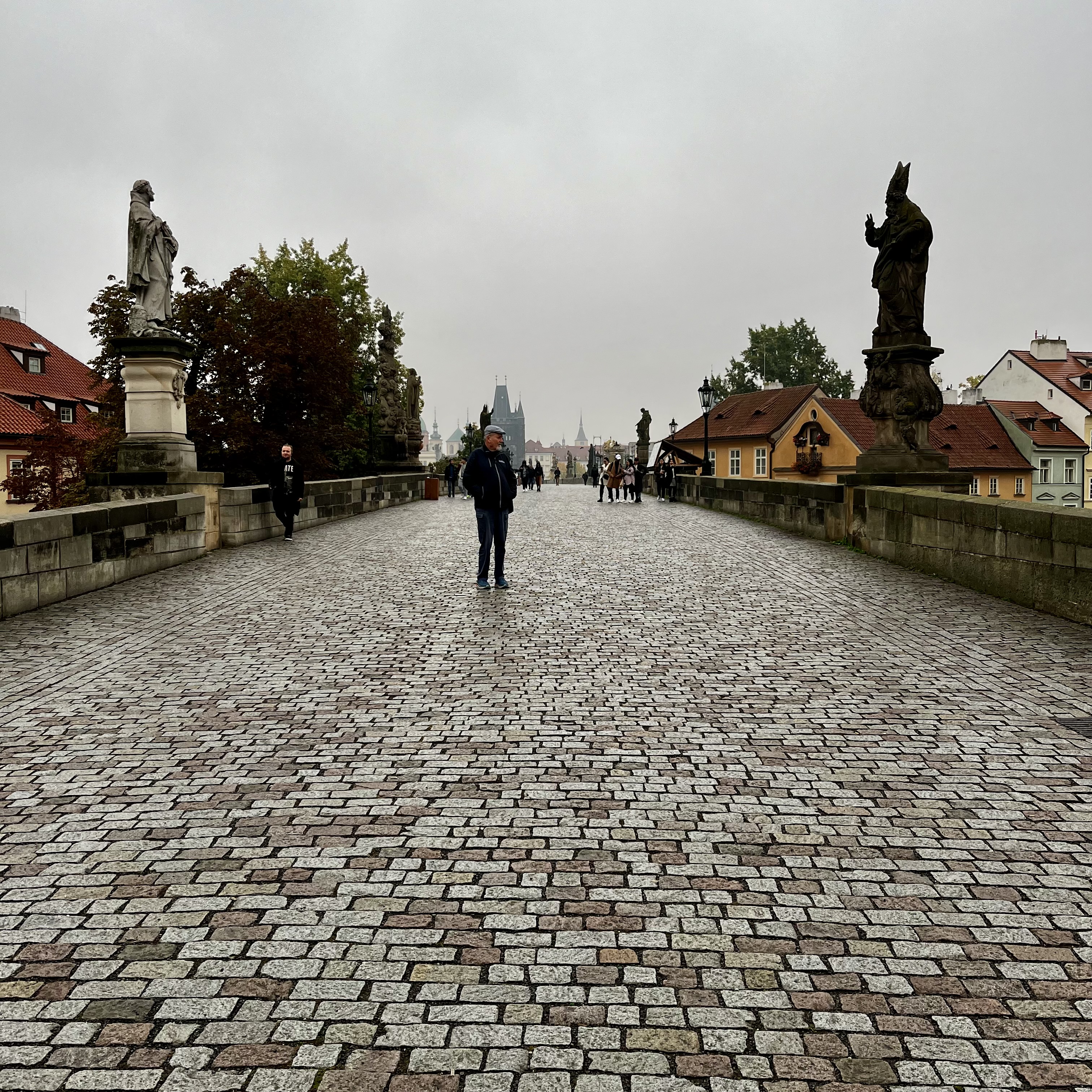 A man standing on the Chales Bridge under the gray clouds.